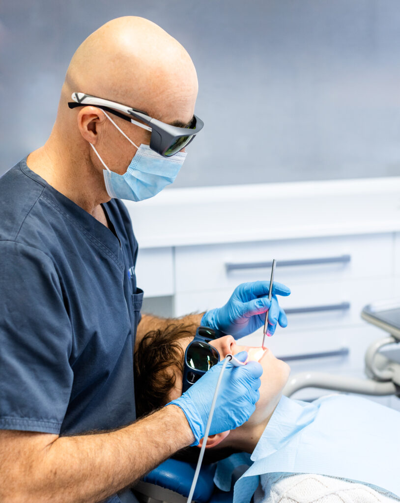 Zdjęcie przedstawia stomatologa podczas użycia lasera stomatologicznego